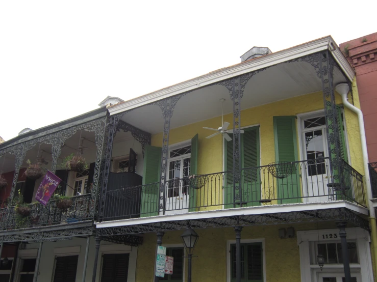 a yellow house with black ironwork balcony and green shutters