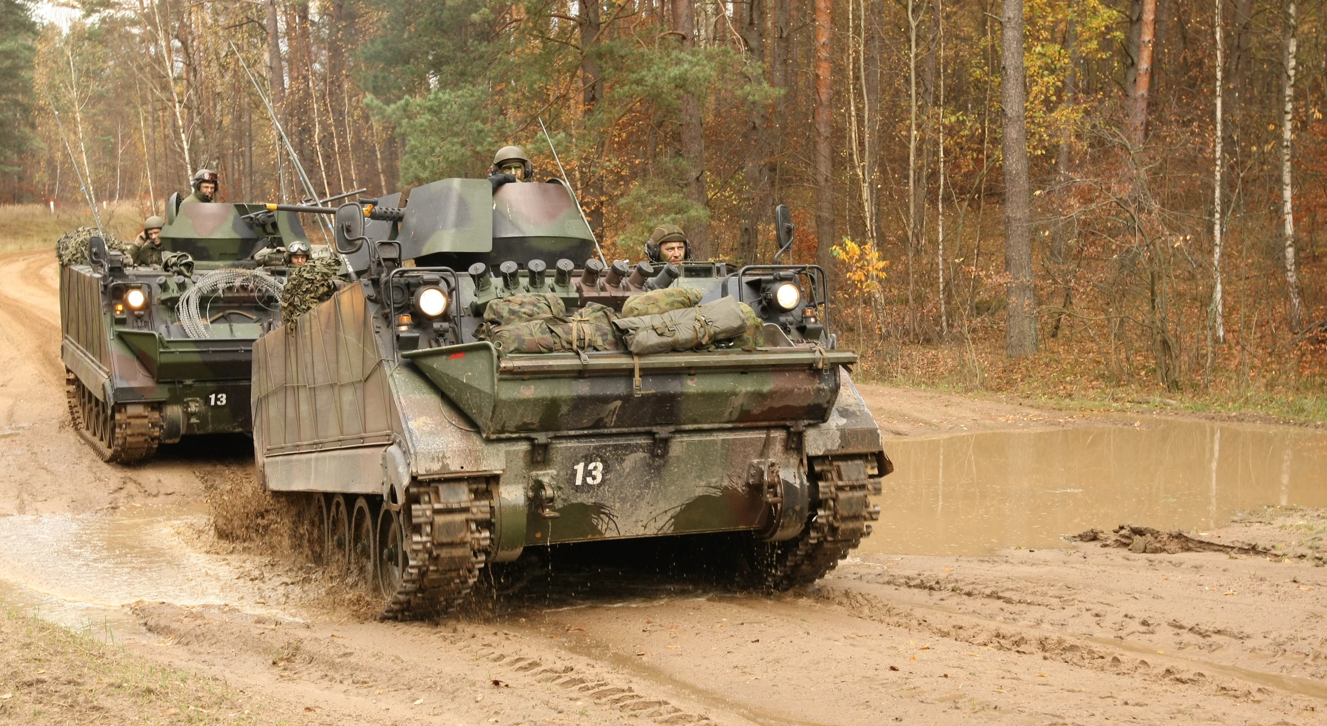 two army vehicles are driving through a muddy road