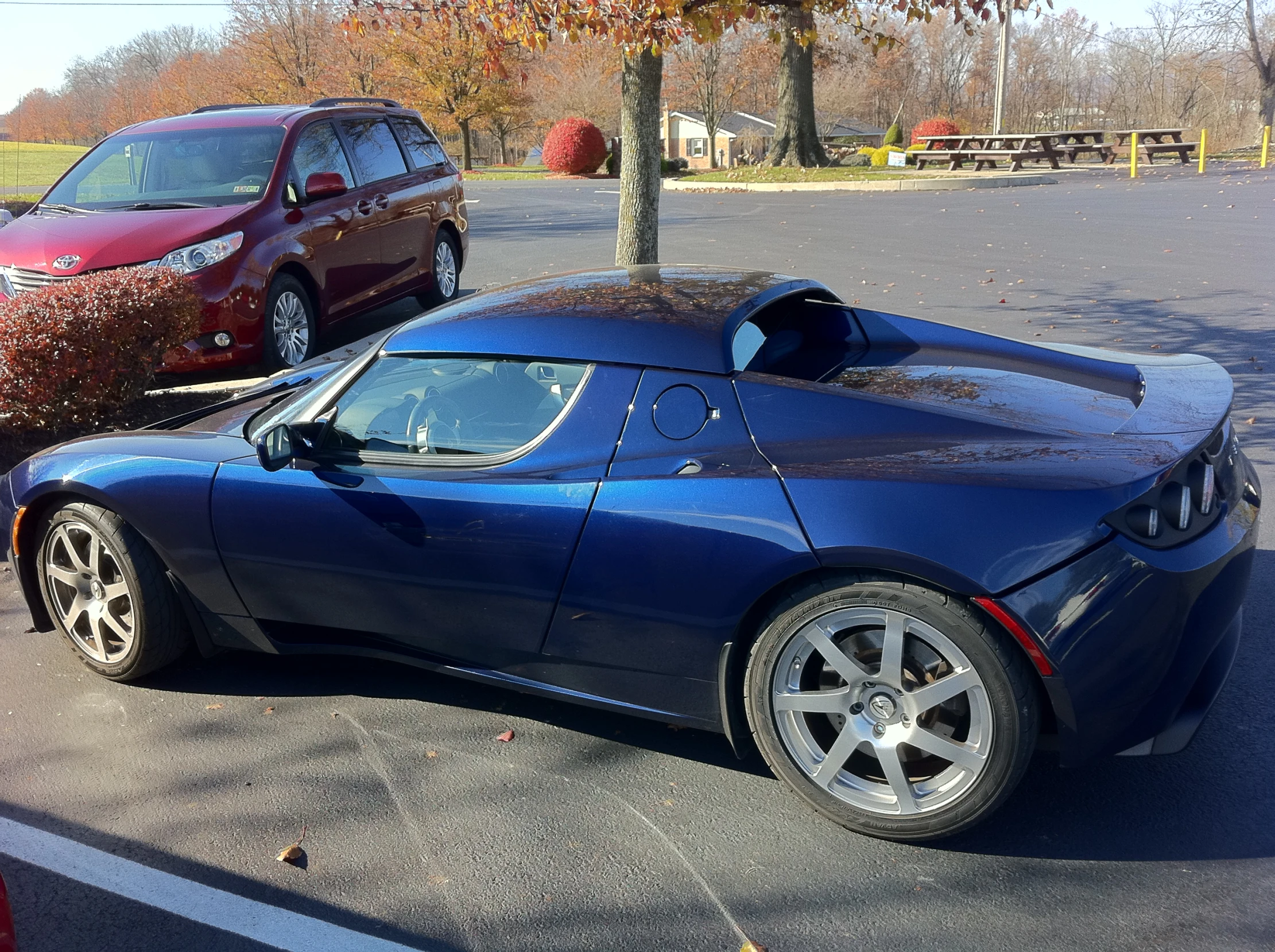 a blue sports car parked in front of a park bench