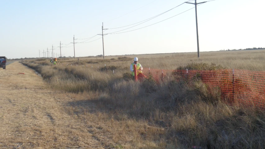 several utility workers in the field with some wires in the background