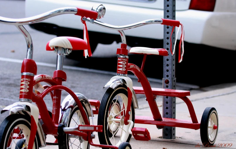 two red tricycles with one standing up and the other sitting down