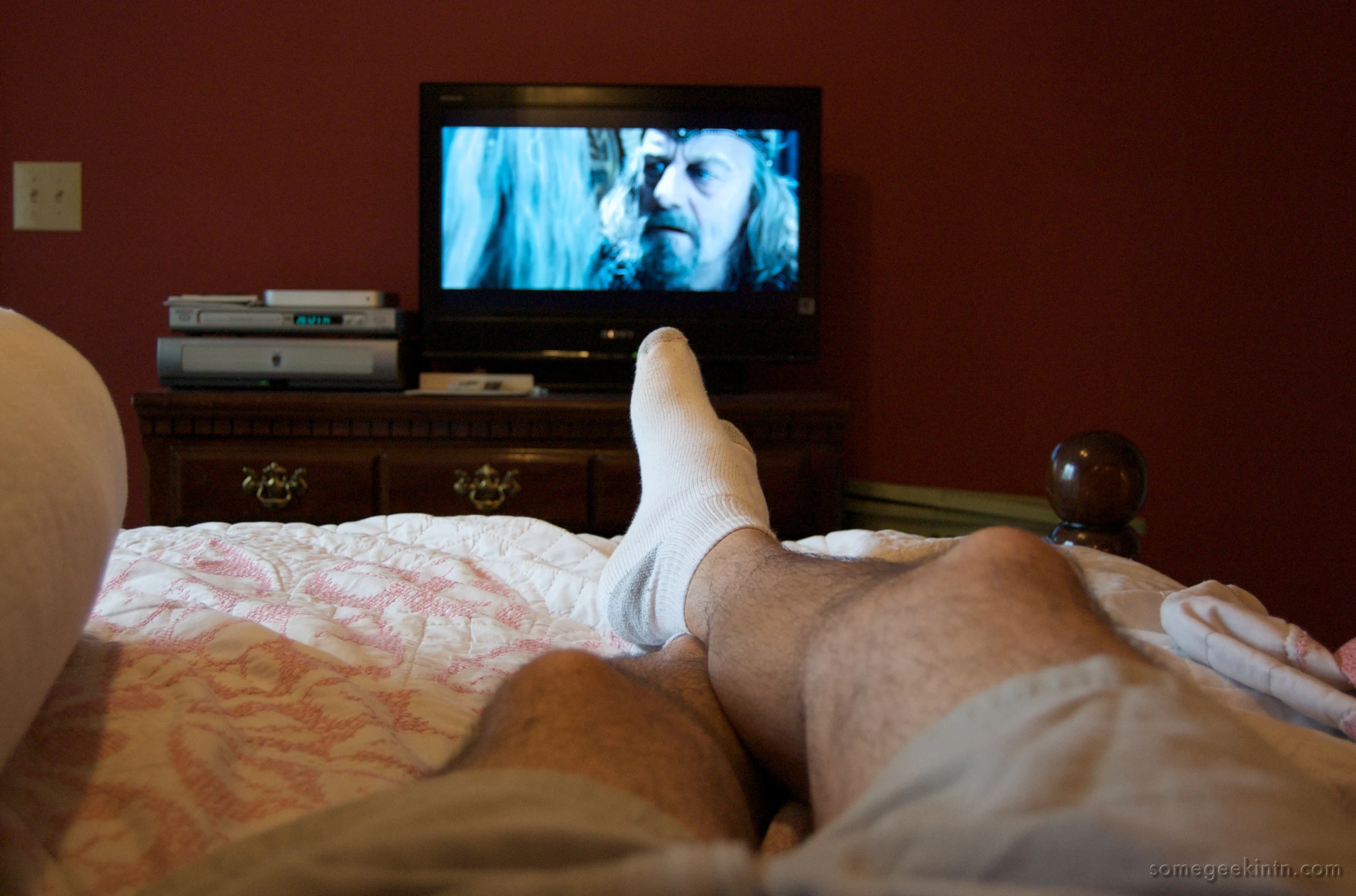 a man lying in bed watching a movie on television