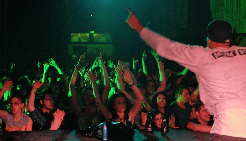 a man in front of a crowd at a concert raising his arms