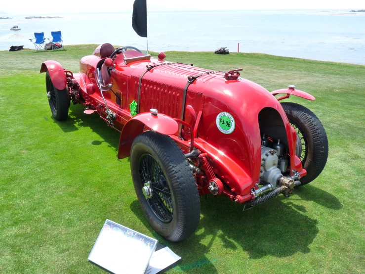 red sports car on display in field next to water