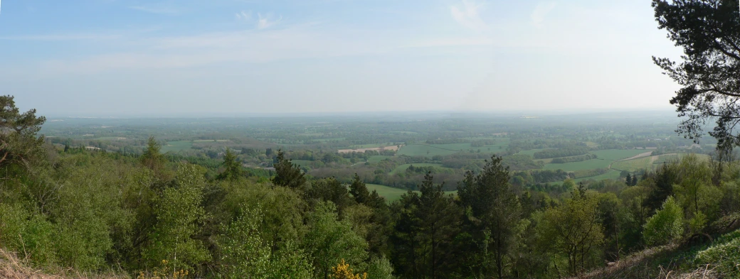 the view out from a hill overlooking a wide valley and tree - lined forest