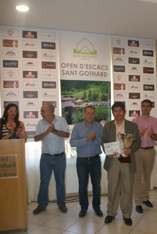 a group of people standing at a podium in front of a wall holding trophies