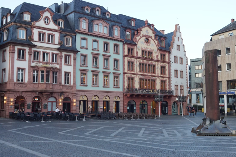 the plaza has multiple buildings on one side and a few tables in the middle