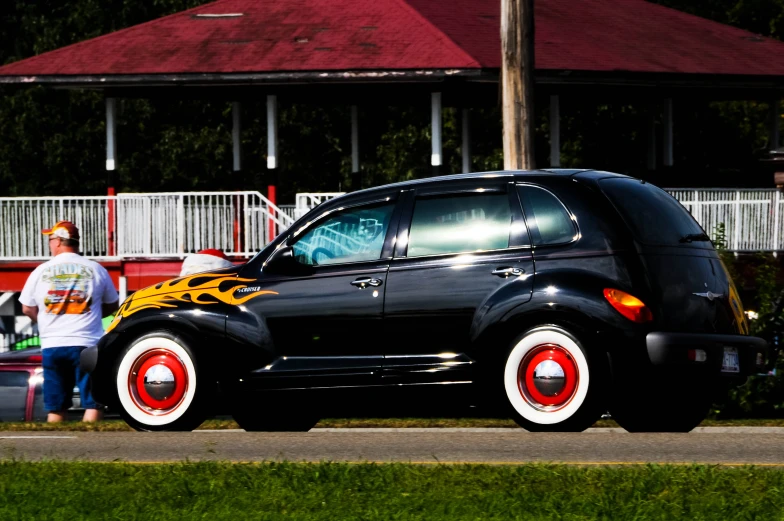 a black, yellow and red car with a man sitting next to it
