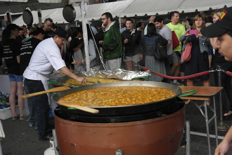 a bunch of people stand near food being cooked