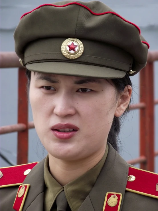 a woman wearing military uniform standing in front of a metal gate