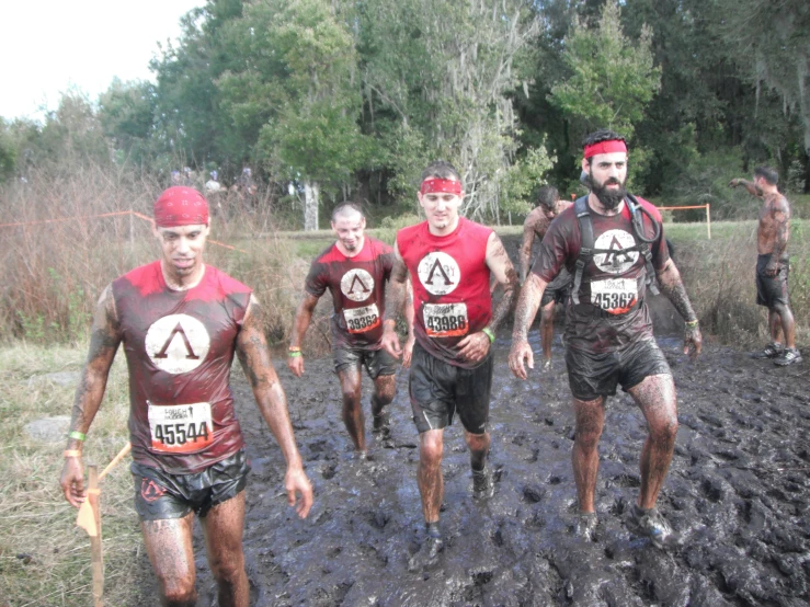 four men are walking in the mud near some trees