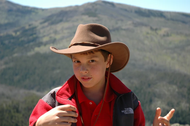 a  standing with a cowboy hat on his head and a mountain in the background