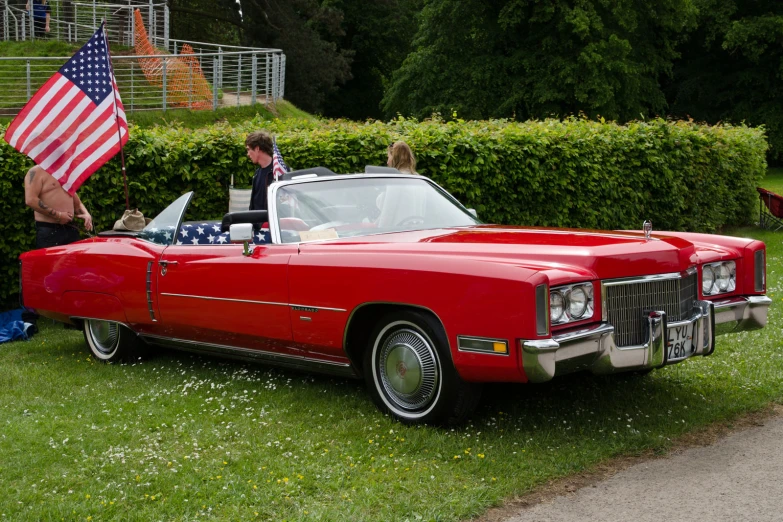 a man and woman in a red convertible with a flag on the hood