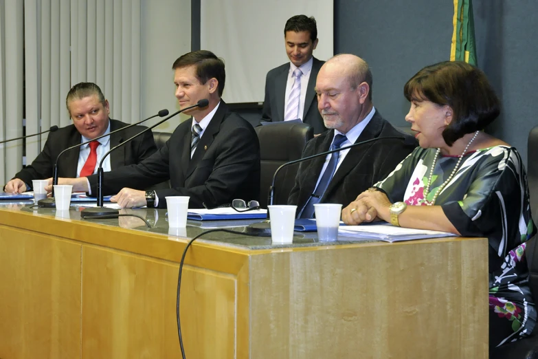 a group of business men sit at a conference table, with microphones and speakers in front of them