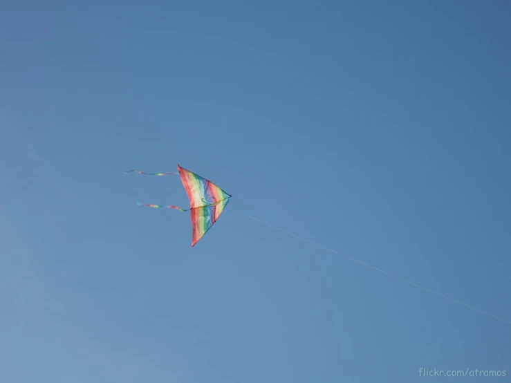a rainbow colored kite flying in the clear blue sky