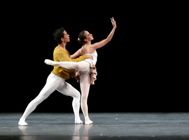 two ballet dancers performing a routine in front of a black background