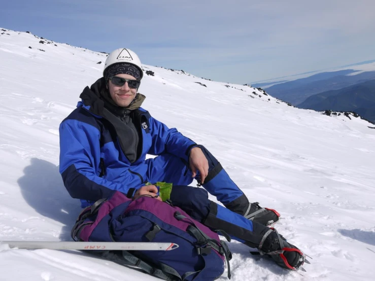 the man with sunglasses sitting in the snow has his legs crossed