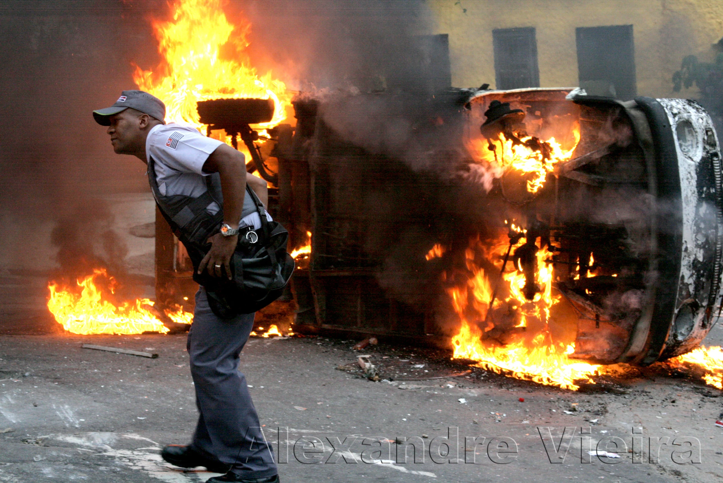 fire burns on a factory and a police officer stands in front