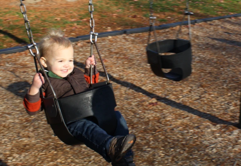 a young child sitting on a swing next to another child