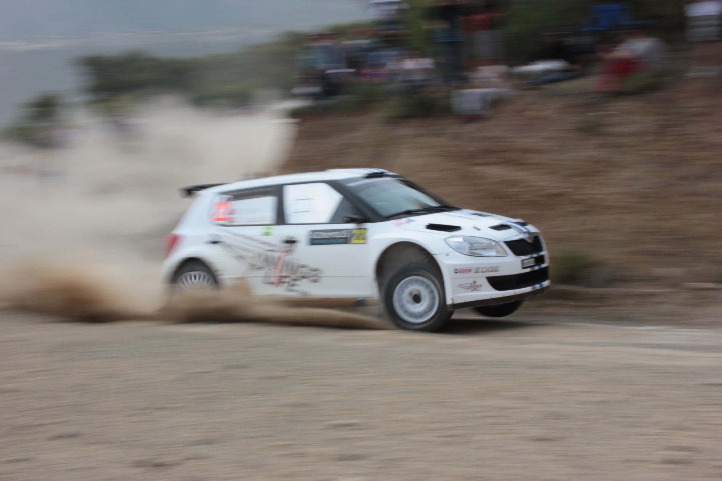 a white vehicle driving on dirt near a hill