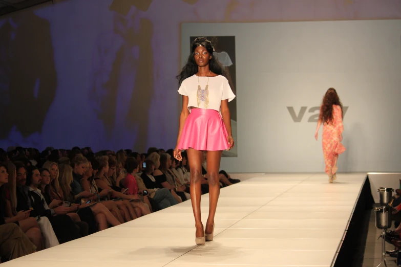 a woman wearing a pink skirt and white top is on the runway