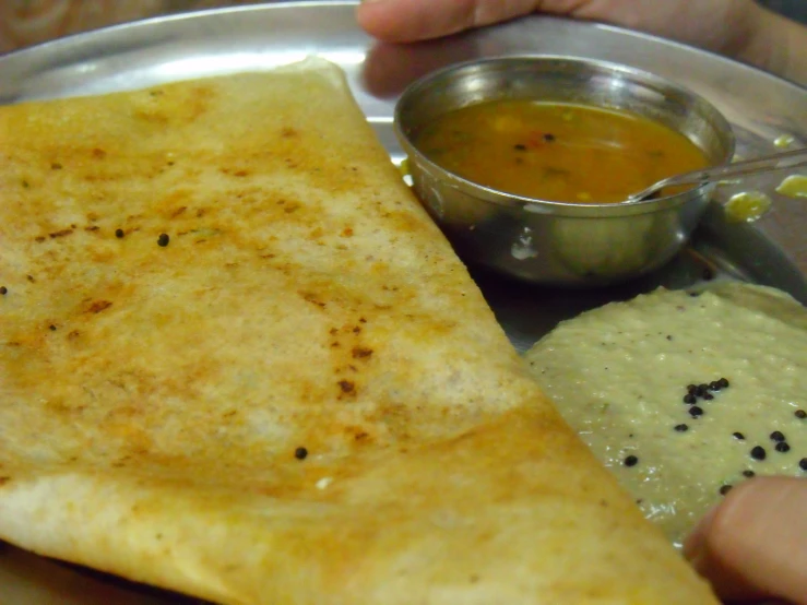 a hand holding a plate that has a pancake and a dip