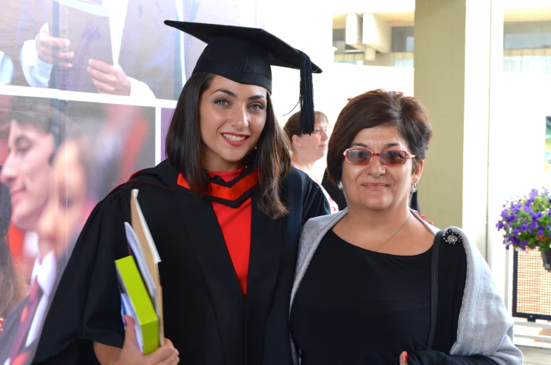 two women smile while posing for a po with her graduation gown