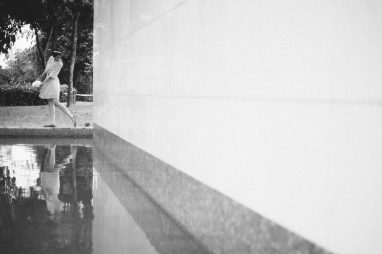 a black and white image of a woman walking past a water fountain