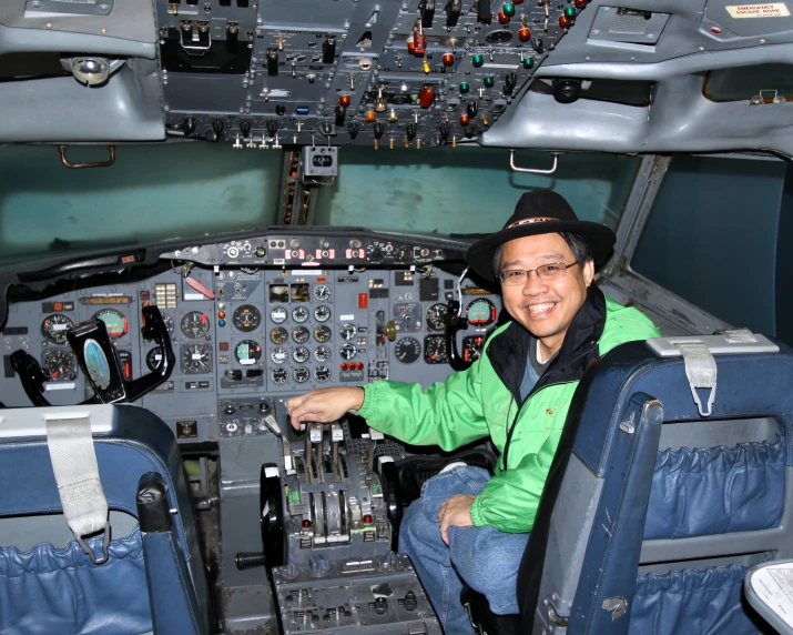 an asian man smiles while sitting in the cockpit of a plane