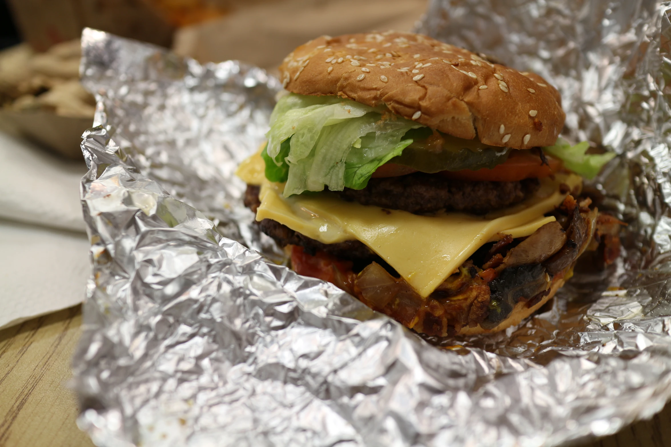 a cheeseburger with lettuce and tomatoes sitting on aluminum foil