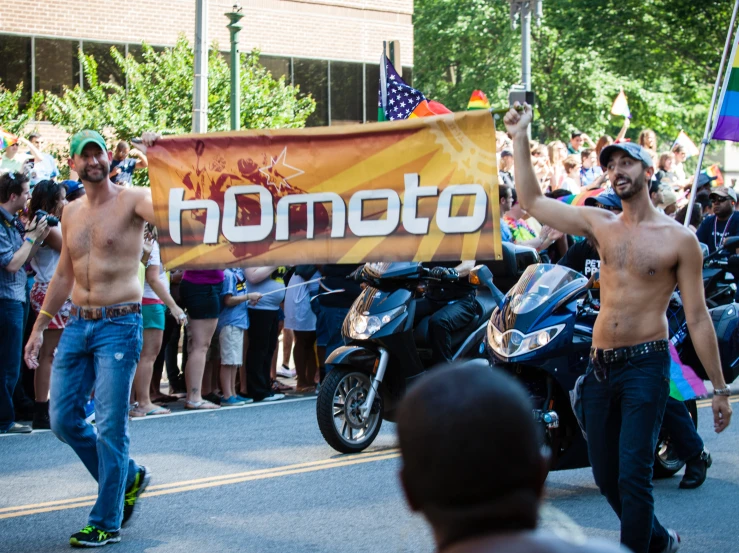 three men are running down the road and there is a banner that reads homo on it
