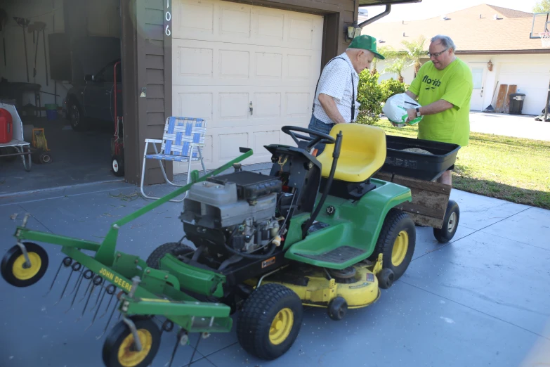 two men standing near a green tractor with a grass catcher on it