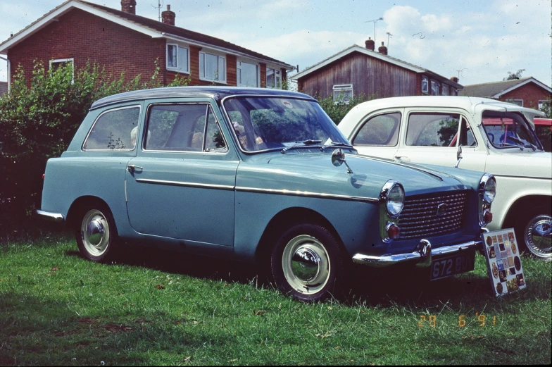 two vintage automobiles parked on a lawn in front of houses