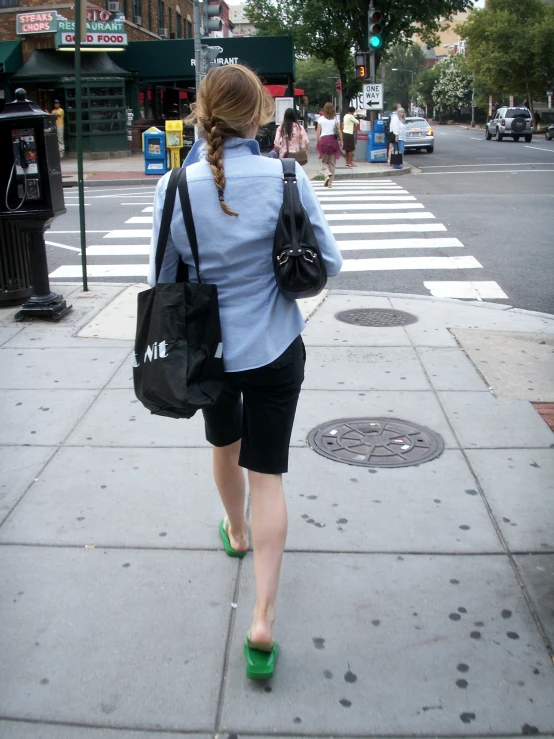 woman wearing sandals and carrying a black bag crosses the street