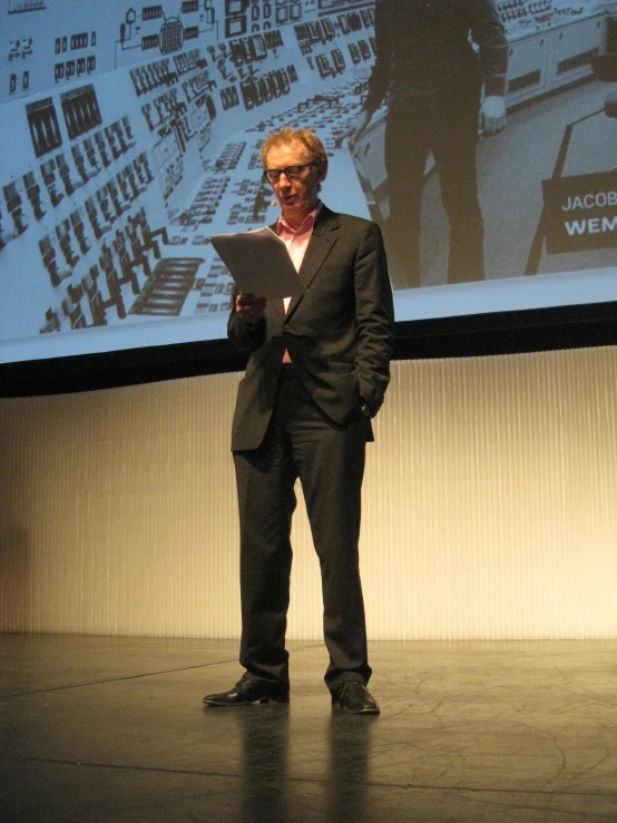 man in black suit and white shirt on stage at a presentation