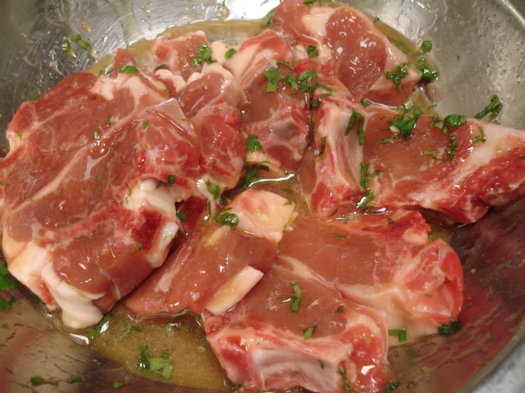 raw meat cooking in an aluminum pan with some herbs