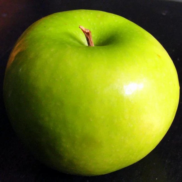 a green apple sitting on top of a black table