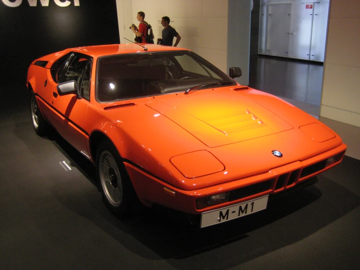 orange bmw sports car displayed in museum with people standing nearby