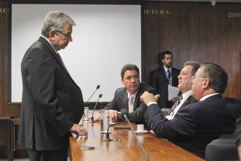 a group of men sitting around a wooden table with microphones