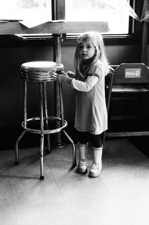 a little girl holding on to a stool