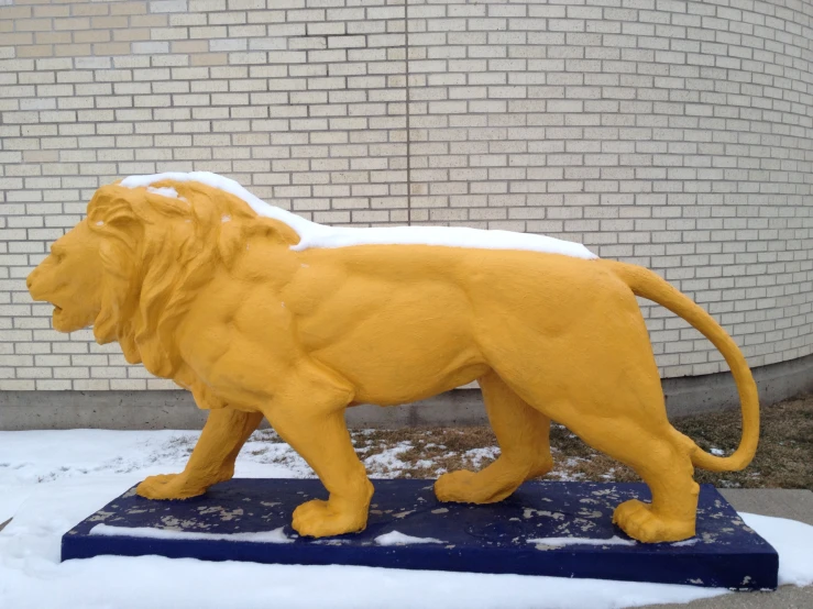 a yellow statue of a lion is in the snow