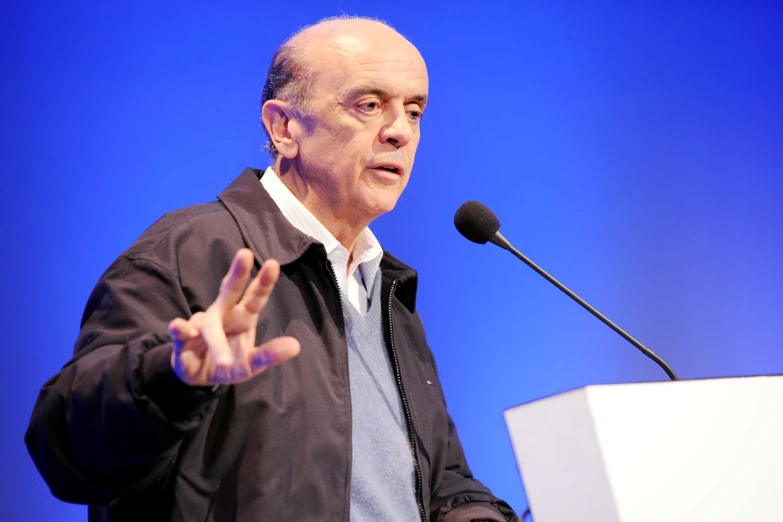 an older man standing behind a podium with his hands in front of him