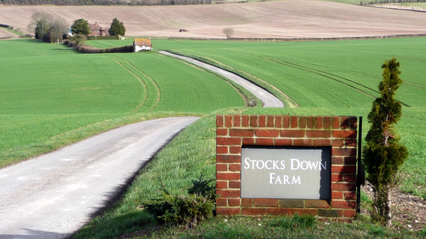 brick sign with road leading to farm in distance