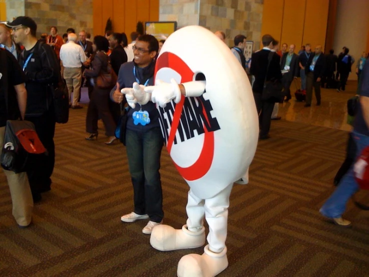 many people stand around in a lobby and are in large costumes with giant balloons, holding kites