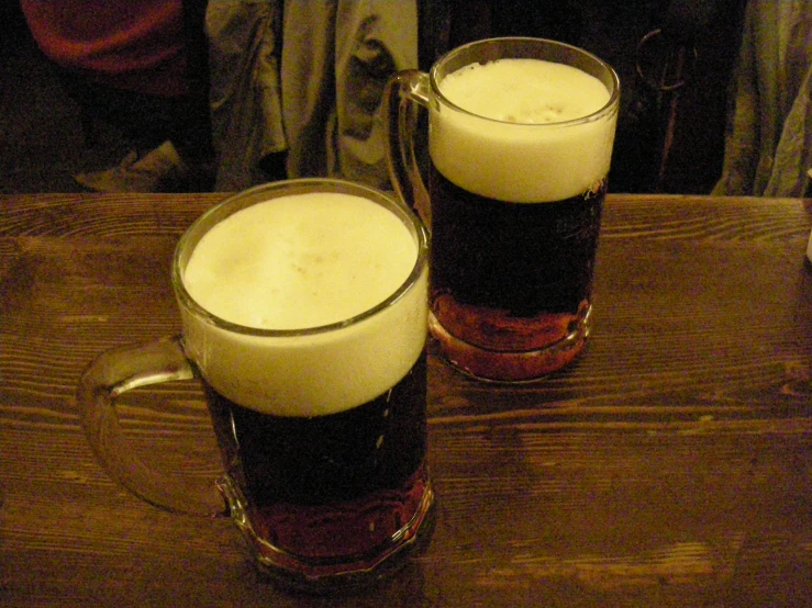 two glasses of beer sit on the table next to each other