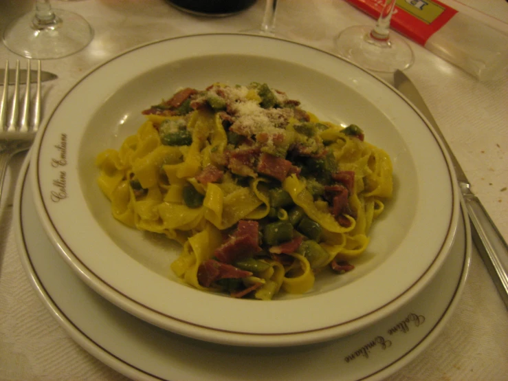 a white plate holding a pasta with ham, vegetables and cheese