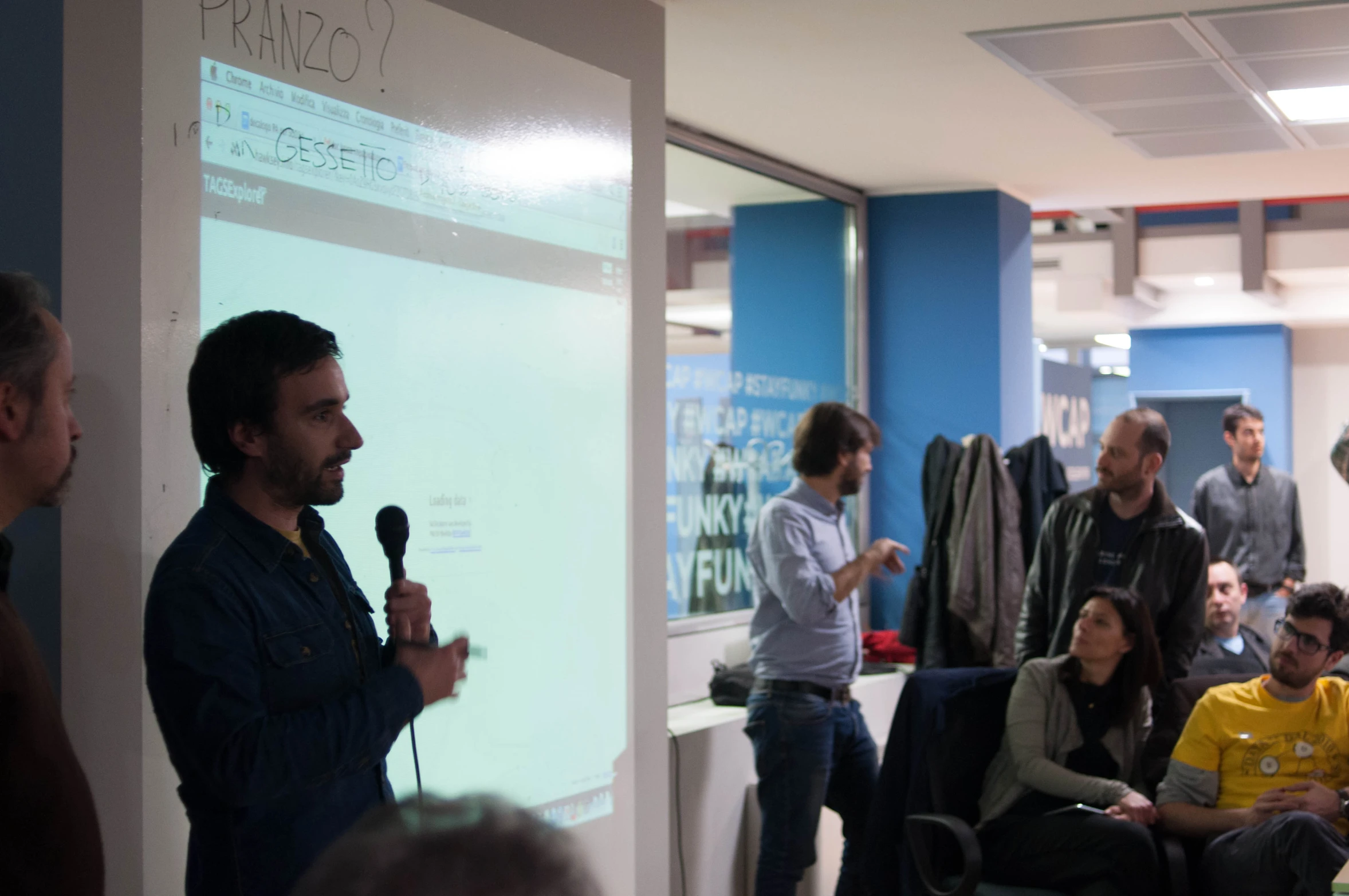 a man stands in front of a white board while another man is holding a microphone