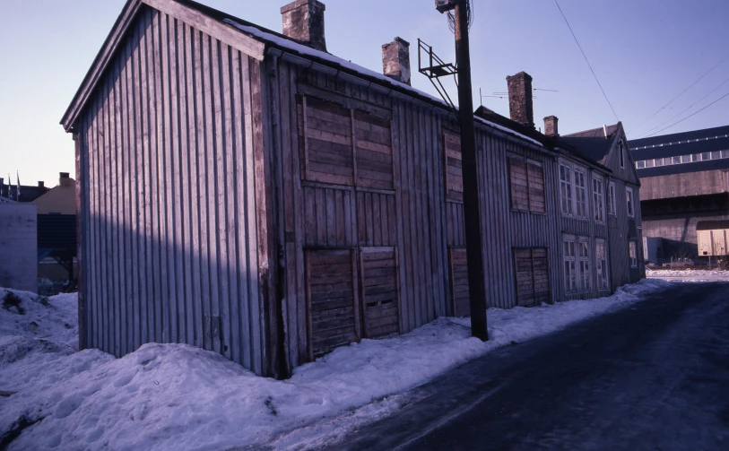 an old style shack with snow on the ground and electrical poles by it