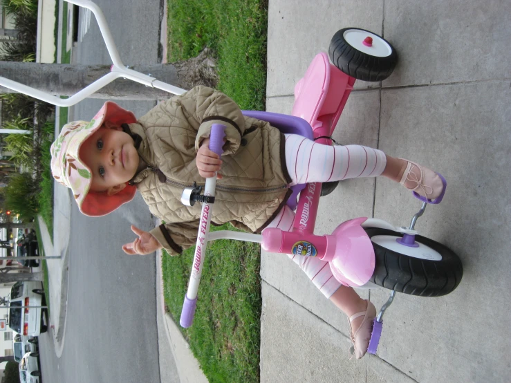 a little girl on the sidewalk playing with a toy scooter
