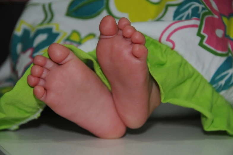 a very small baby feet covered by a green blanket